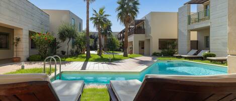 A pool area with lounge chairs, palm trees, and a clear blue sky.