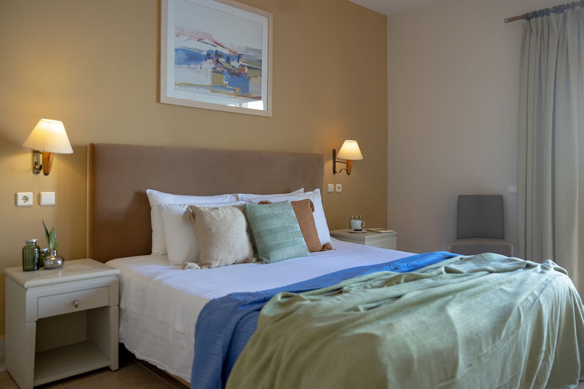 Ein Hotelzimmer mit einem großen Bett, zwei Nachttischen, einem Beistelltisch, einem Sessel und einem Bild an der Wand.