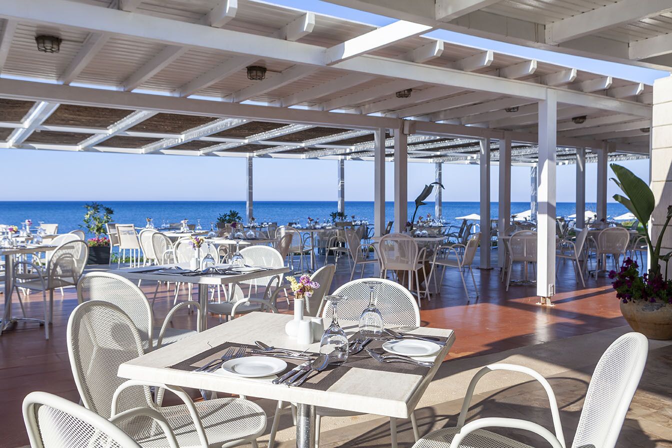 An outdoor dining area with tables and chairs, overlooking the sea.