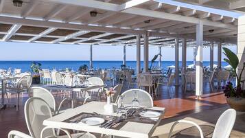 An outdoor dining area with tables and chairs, overlooking the sea.