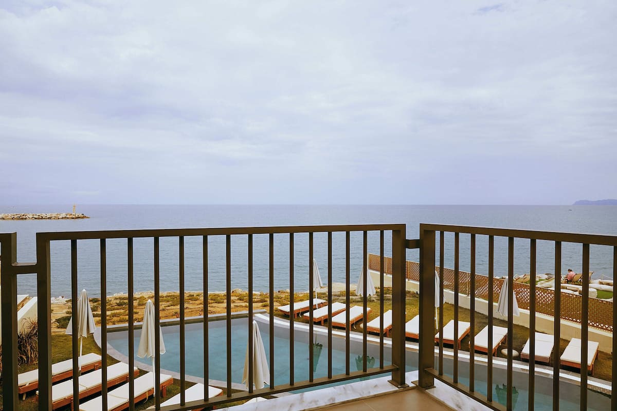 Ein Poolbereich mit Liegestühlen und Sonnenschirmen, Blick aufs Meer und ein Balkon mit Sichtschutz.