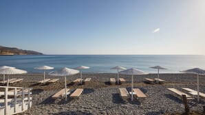A pebble beach with sun loungers and umbrellas, overlooking a calm sea. - Giannoulis – Grand Bay Beach Resort - Adults Only (Platanias)