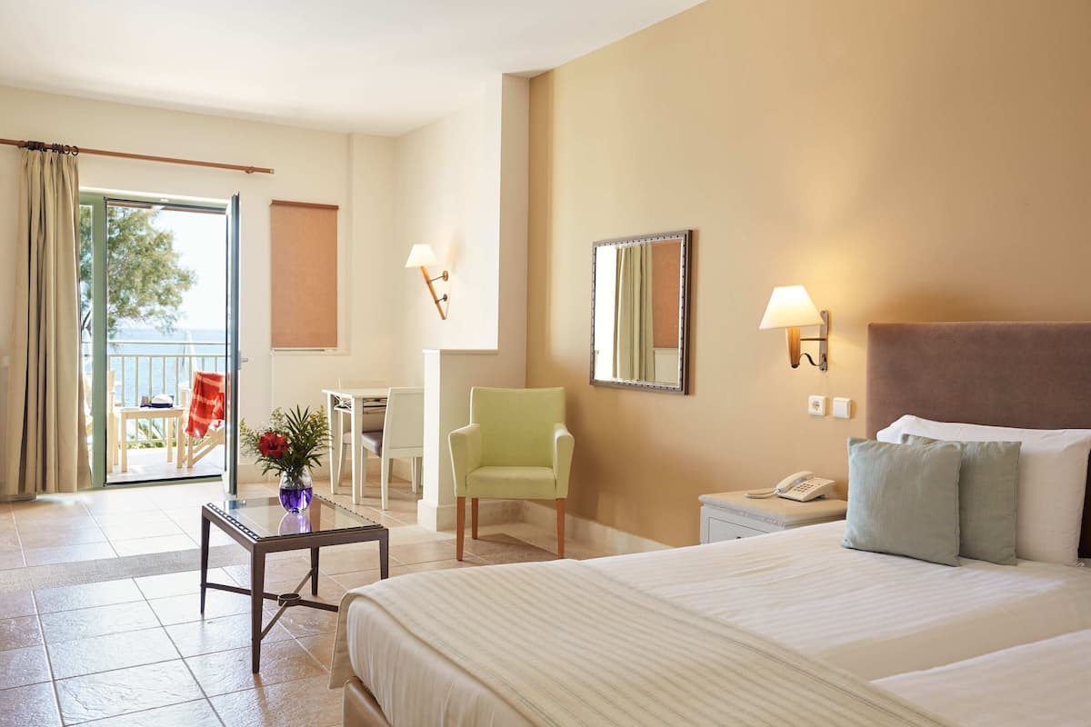 Ein Hotelzimmer mit Bett, Sessel, kleinem Tisch, Nachttisch, Telefon und einem Balkon mit Stuhl und Tisch.