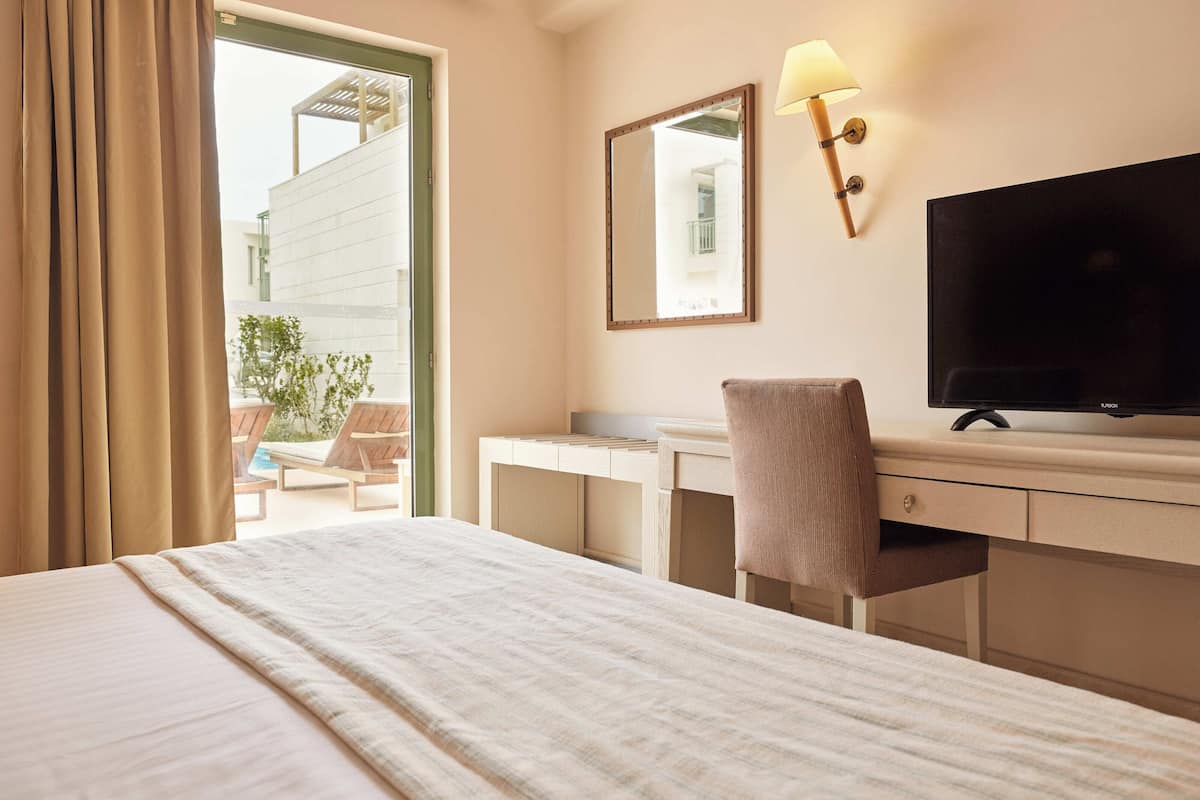 Ein Hotelzimmer mit Bett, Schreibtisch mit Stuhl, Fernseher, Spiegel und einem Fenster mit Vorhängen.