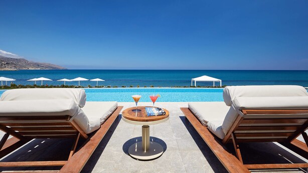 A poolside lounge area with two sun loungers, a small round table with drinks, and a view of the sea. - Giannoulis – Grand Bay Beach Resort - Adults Only (Platanias)