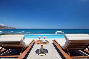 A poolside lounge area with two sun loungers, a small round table with drinks, and a view of the sea. - Giannoulis – Grand Bay Beach Resort - Adults Only (Platanias)