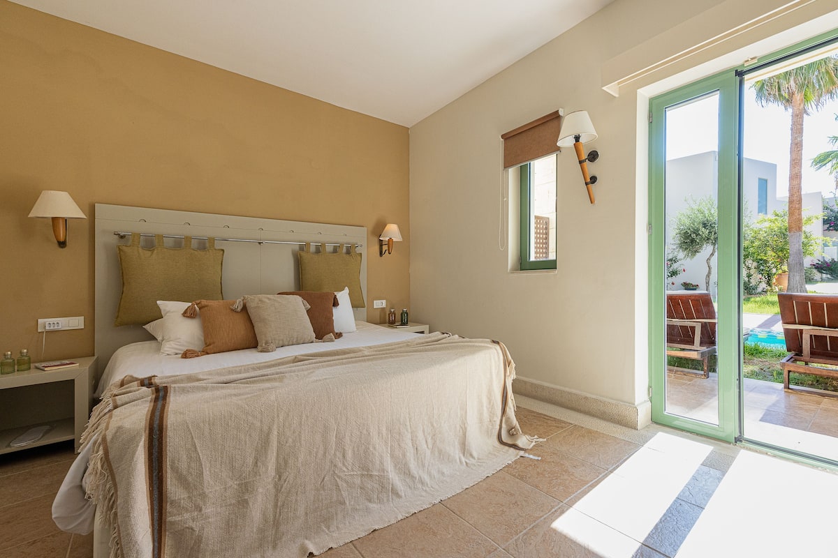 Ein Hotelzimmer mit einem großen Bett, zwei Nachttischen, einem Fenster mit Blick ins Freie und einer Tür zu einem Balkon.