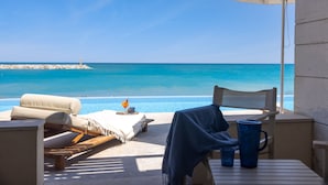 A seaside lounge with a view of the ocean, a table with a blue mug, and a chair with a towel. - Giannoulis – Grand Bay Beach Resort - Adults Only (Platanias)