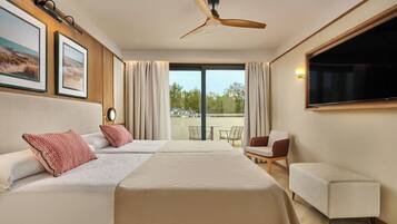 Habitación de hotel con cama, dos almohadas, ventilador de techo, televisor y balcón con sillas.