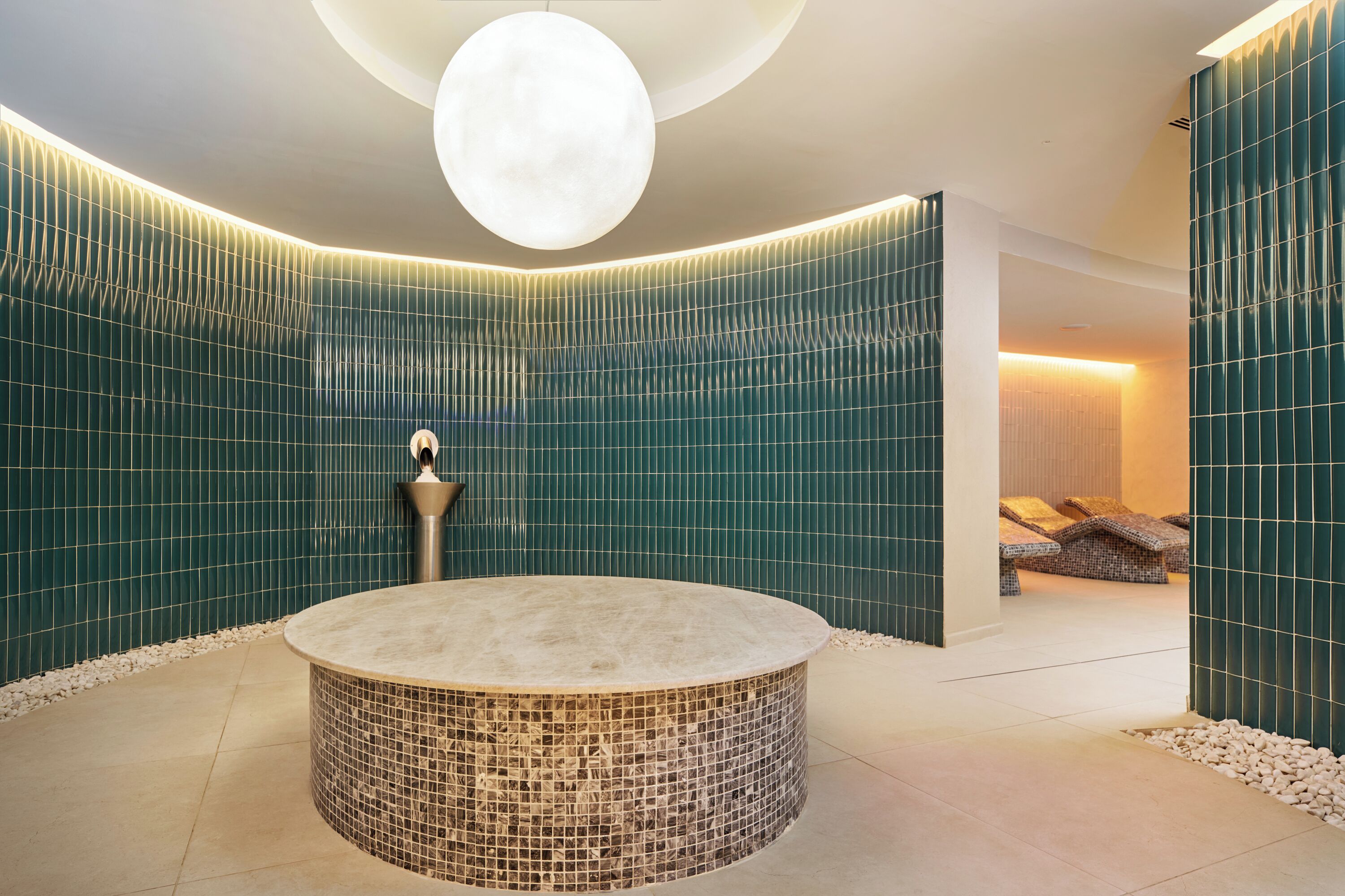A spa room with a circular hot tub, a wall-mounted light fixture, and a seating area with cushions.