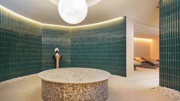 A spa room with a circular hot tub, a wall-mounted light fixture, and a seating area with cushions.