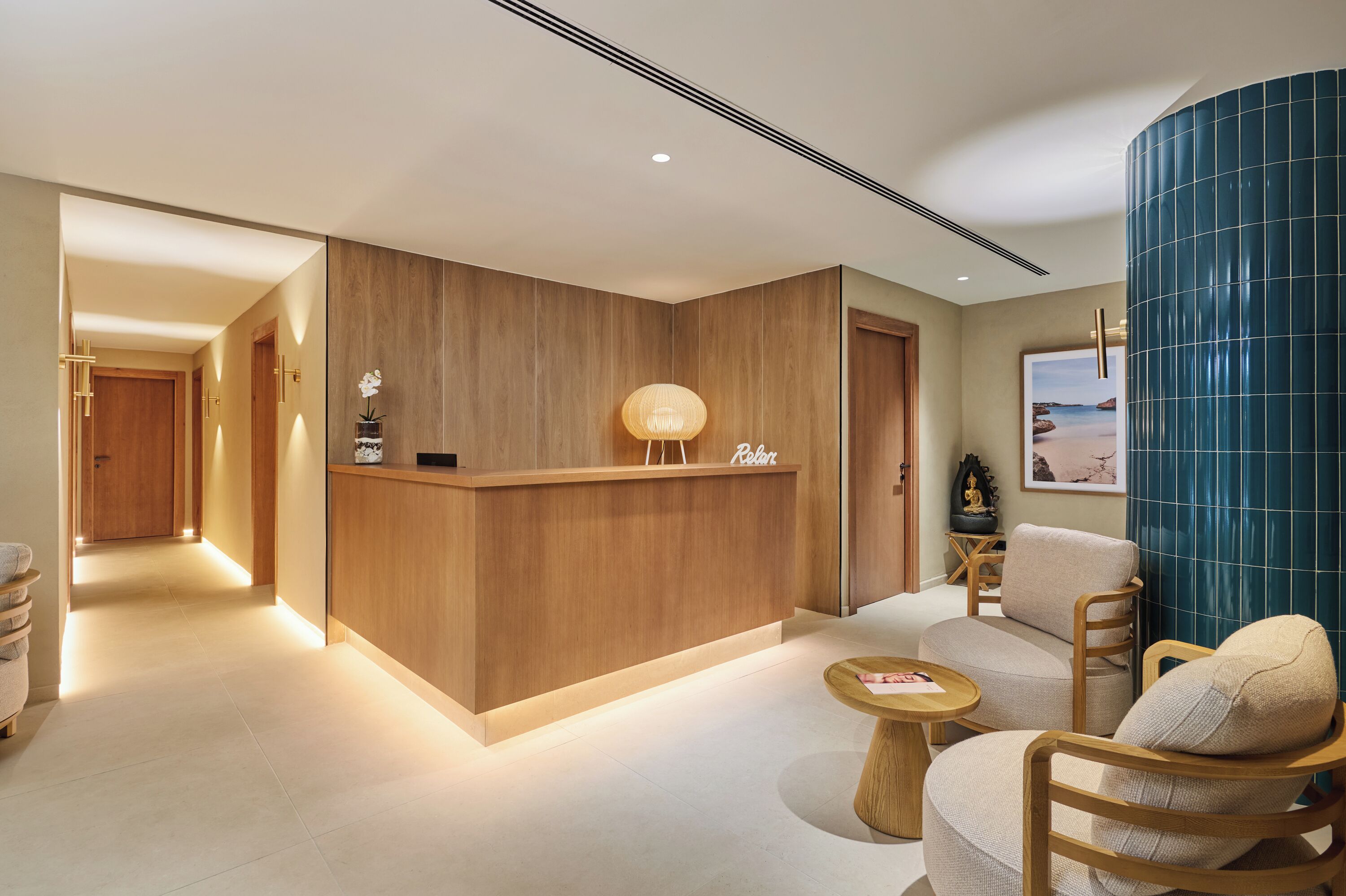 Un mostrador de recepción con detalles de madera, una zona de estar con una mesa redonda de madera y una pared con un diseño de azulejos azules.