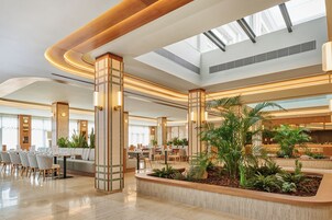 Un amplio vestíbulo de hotel con un área de estar central, varias mesas de comedor y un gran jardín interior.