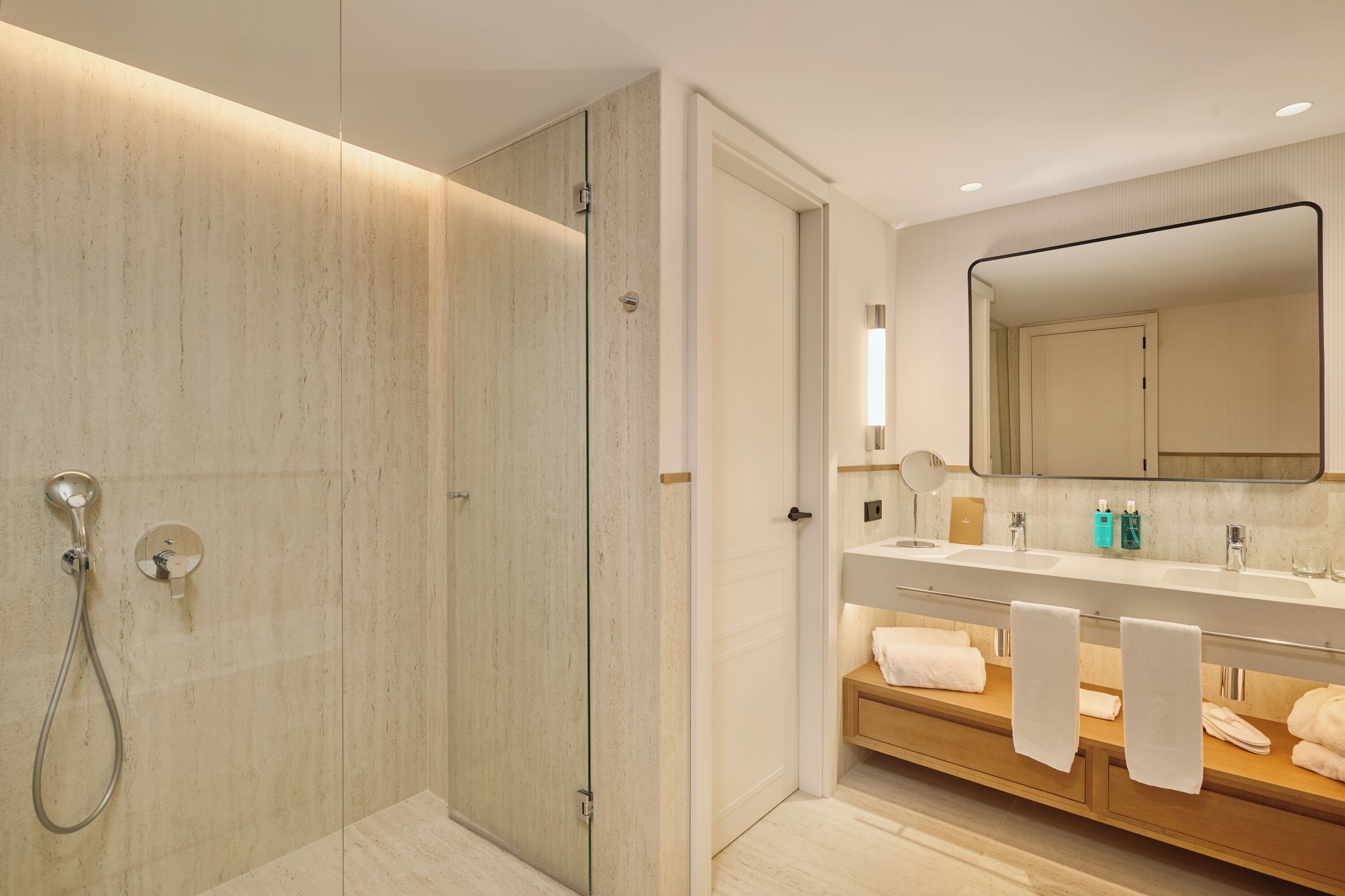 A modern bathroom with a glass-enclosed shower, a vanity with a mirror, and a wooden bench with towels.