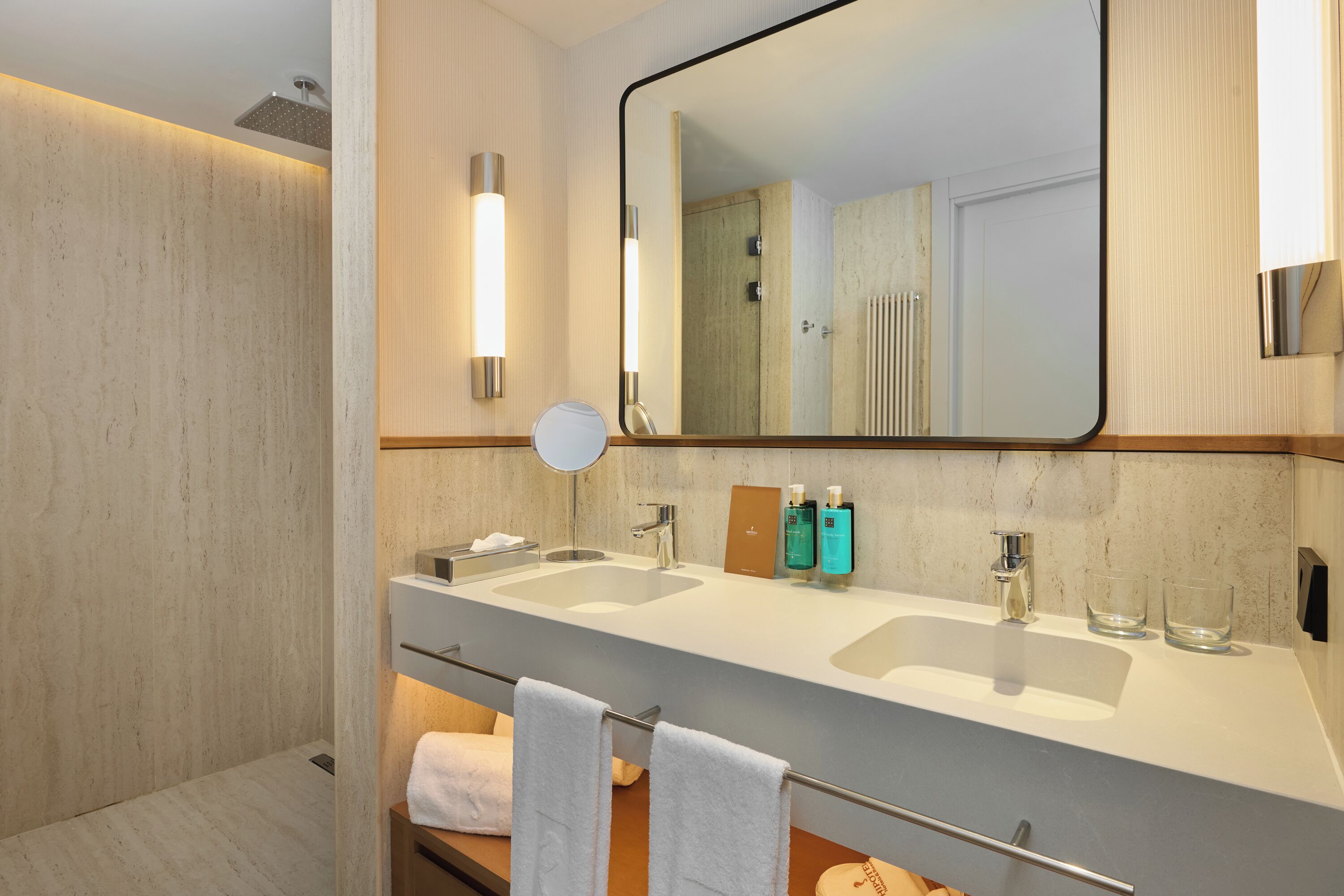 Un baño moderno con dos lavamanos, un espejo grande y un perchero para toallas.