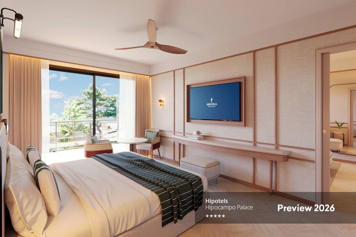 Een moderne hotelkamer met een groot bed, een aan de muur bevestigde televisie, een plafondventilator en een balkon met uitzicht op groen.