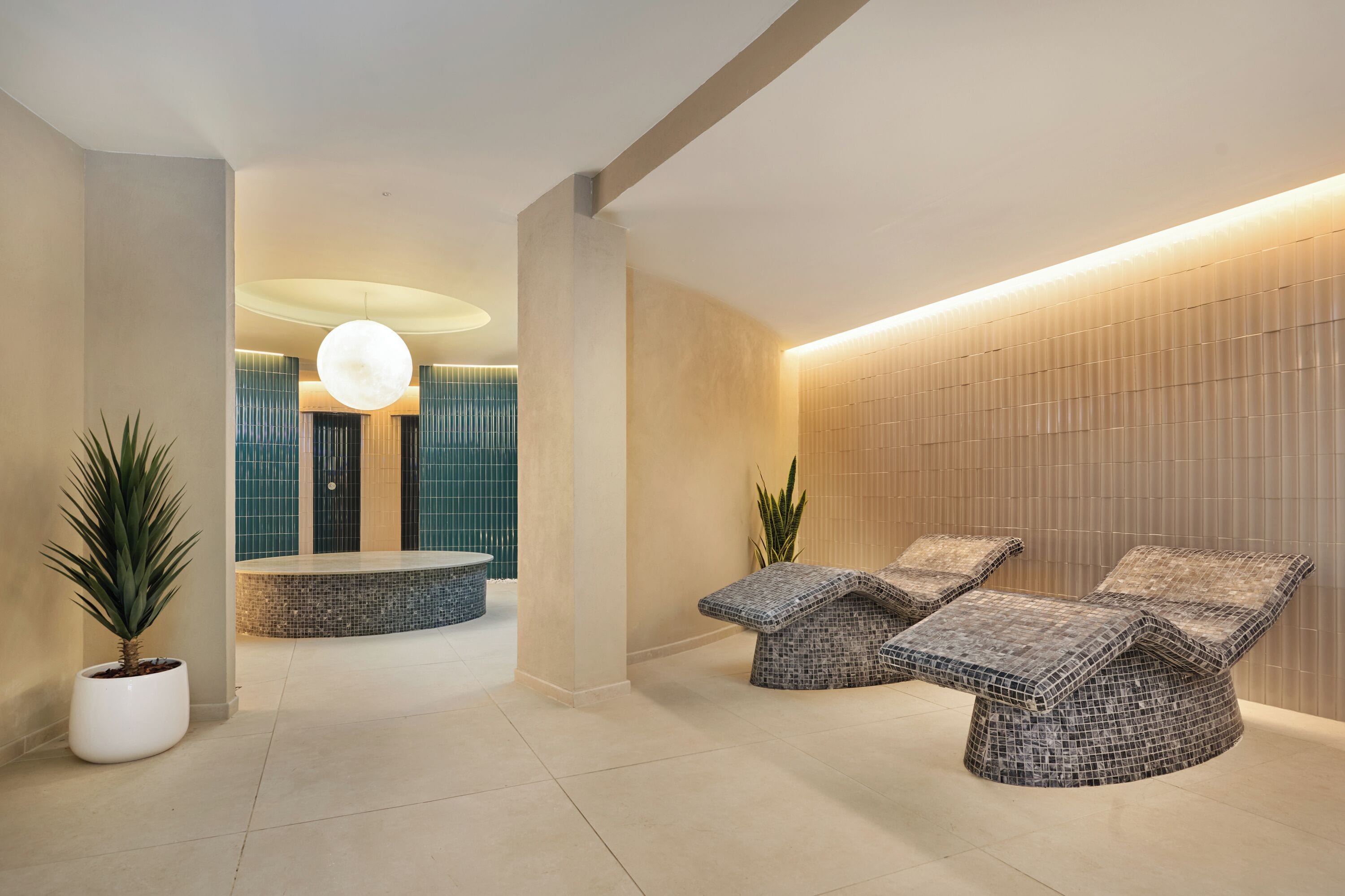 A modern lounge area with a mosaic-tiled seating area, a central round table, and a large hanging light fixture.