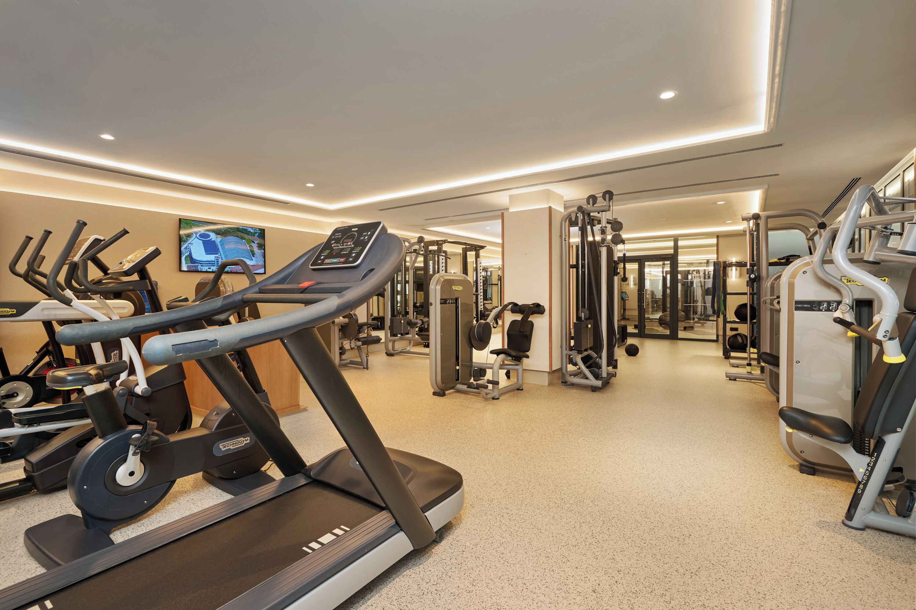 Ein Fitnessstudio mit Laufbändern, Kraftgeräten und einem Fernsehbildschirm, der einen Überblick zeigt.
