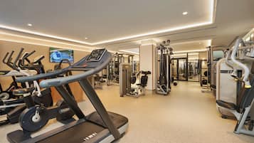 Ein Fitnessstudio mit Laufbändern, Kraftgeräten und einem Fernsehbildschirm, der einen Überblick zeigt.