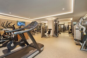 A gym with treadmills, weight machines, and a television screen displaying an aerial view. - Hipotels Hipocampo Palace & Spa (Sant Llorenc des Cardassar)