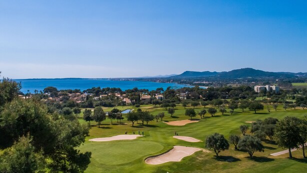 Un parcours de golf agrémenté de bunkers, d’arbres et offrant une vue sur la mer et les montagnes.