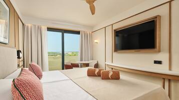 A hotel room with a bed, a TV, a ceiling fan, a window with curtains, and a view of the outdoors.