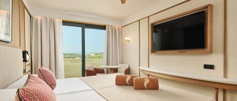 A hotel room with a bed, a TV, a ceiling fan, a window with curtains, and a view of the outdoors.