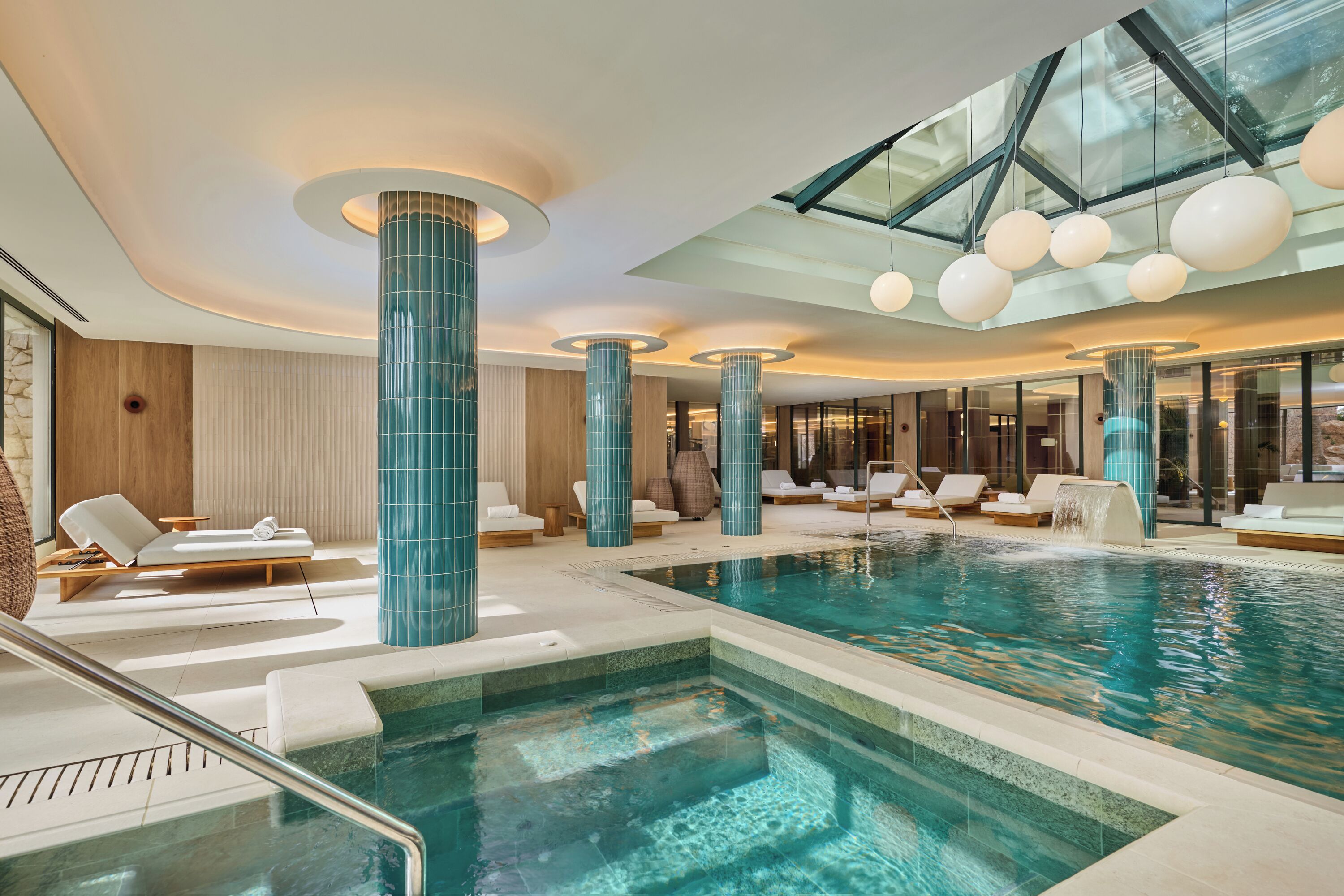 Un área de piscina interior moderna con varias zonas de estar y techo de cristal.