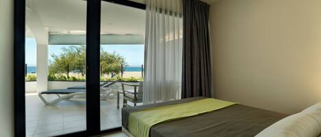 A modern bedroom with a bed, a sliding glass door leading to a balcony with a table and chairs, and a view of the outdoors.