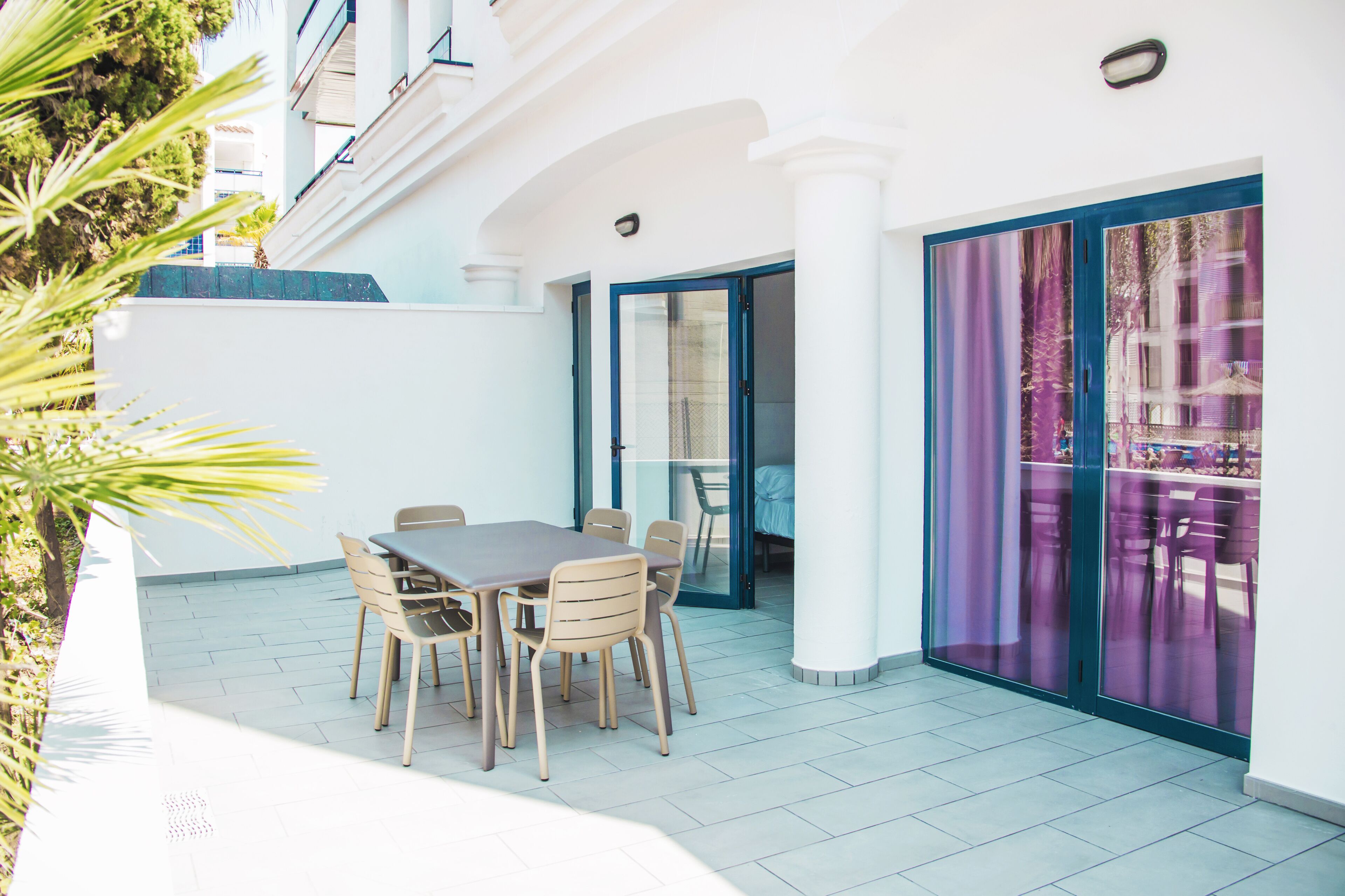 An outdoor patio with a table and chairs, a sliding glass door, and a view of a building with balconies.