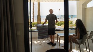 A man standing by a window overlooking a beach, with a woman seated inside.
