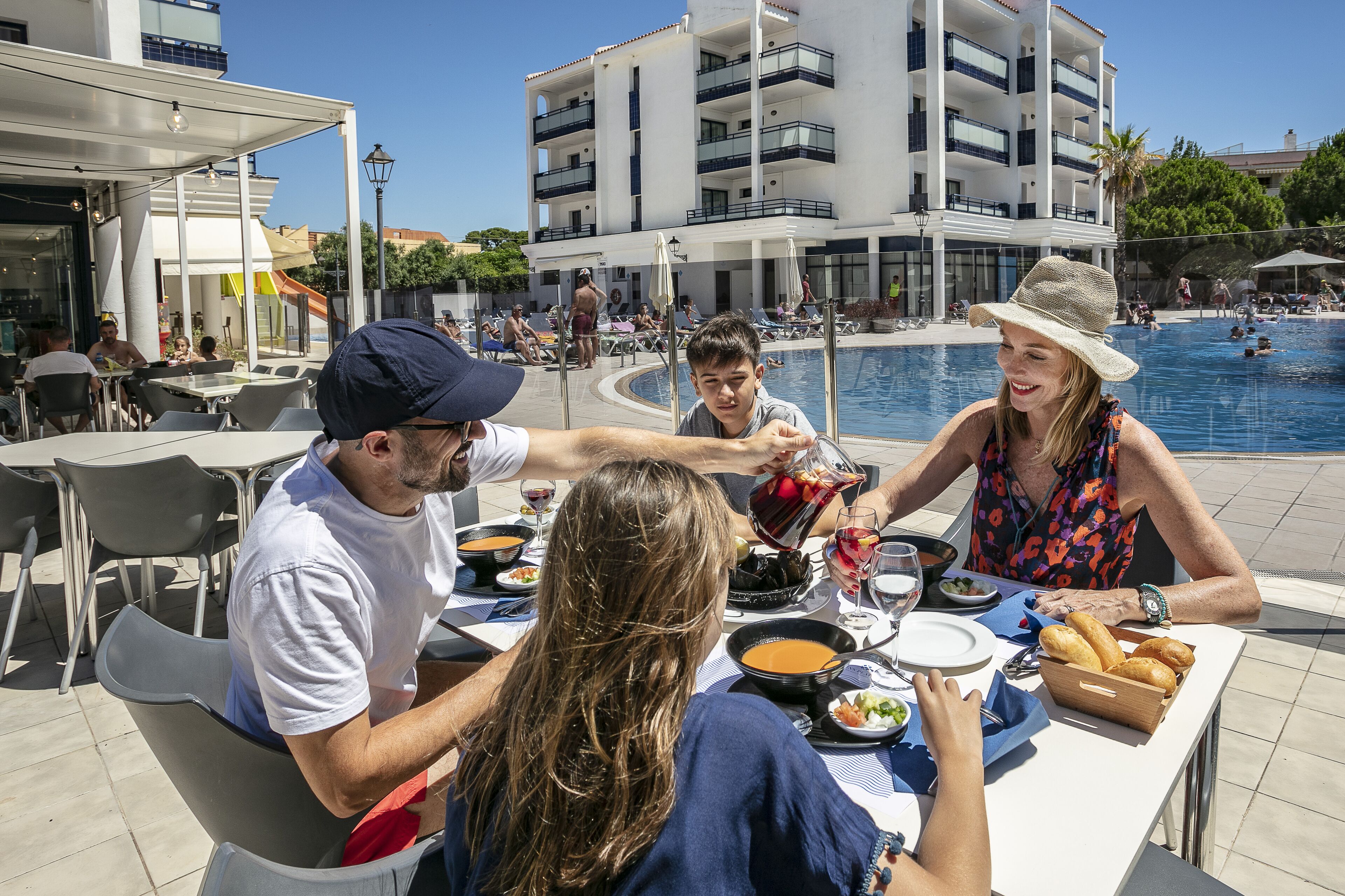 A dining area with tables and chairs, a pool, and a building in the background.