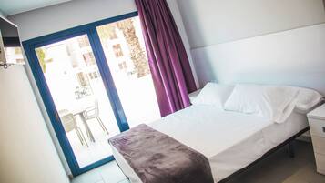 Un dormitorio con cama, mesita de noche y ventana con cortinas.