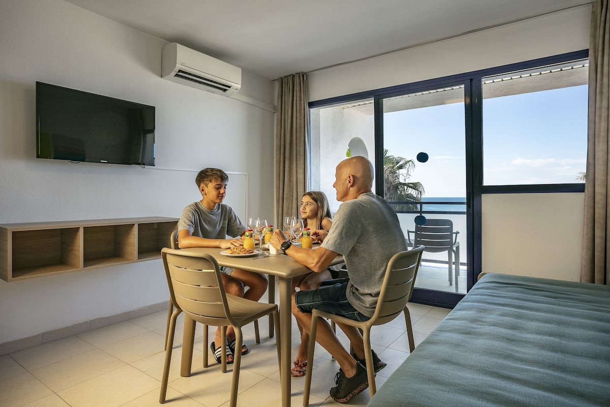 A modern dining area with a flat-screen TV, a large window with a view of the sea, and a balcony with outdoor furniture.