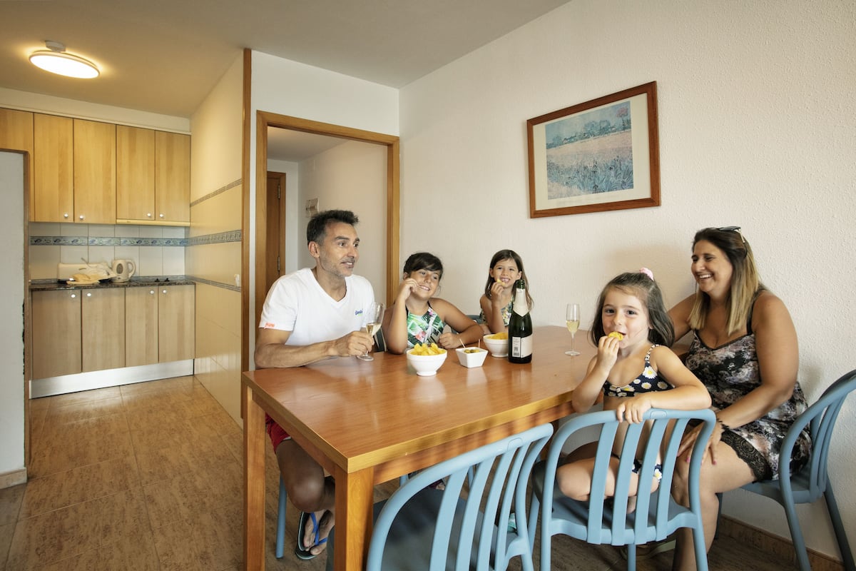 A family dining at a wooden table in a room with a kitchen in the background.