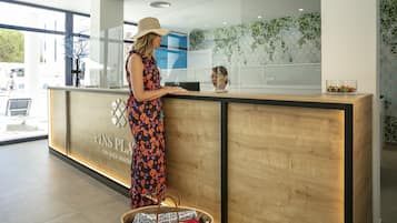 Un mostrador de recepción con un logotipo, una mujer de pie detrás y una cesta con revistas.