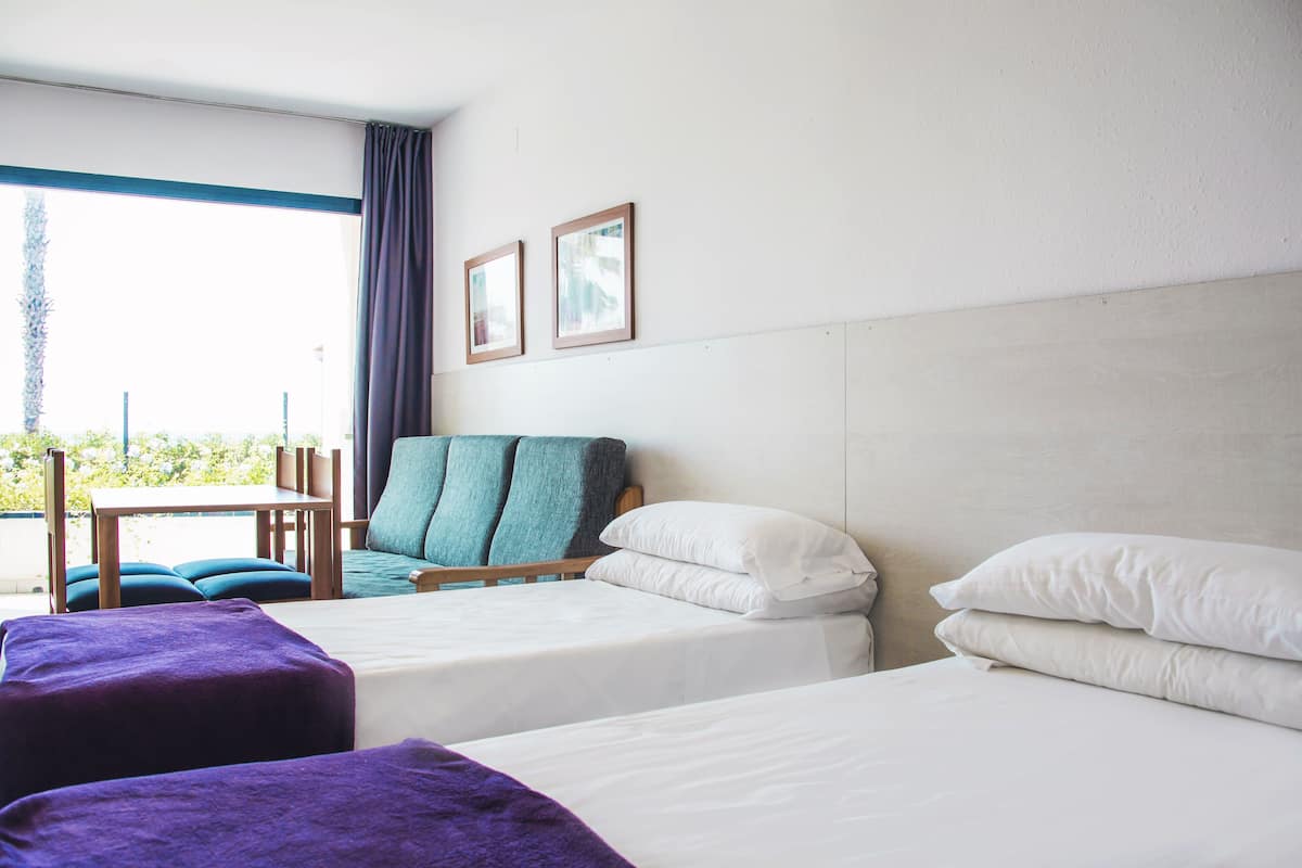 A hotel room with two beds, a chair, a table, and a view of greenery outside.