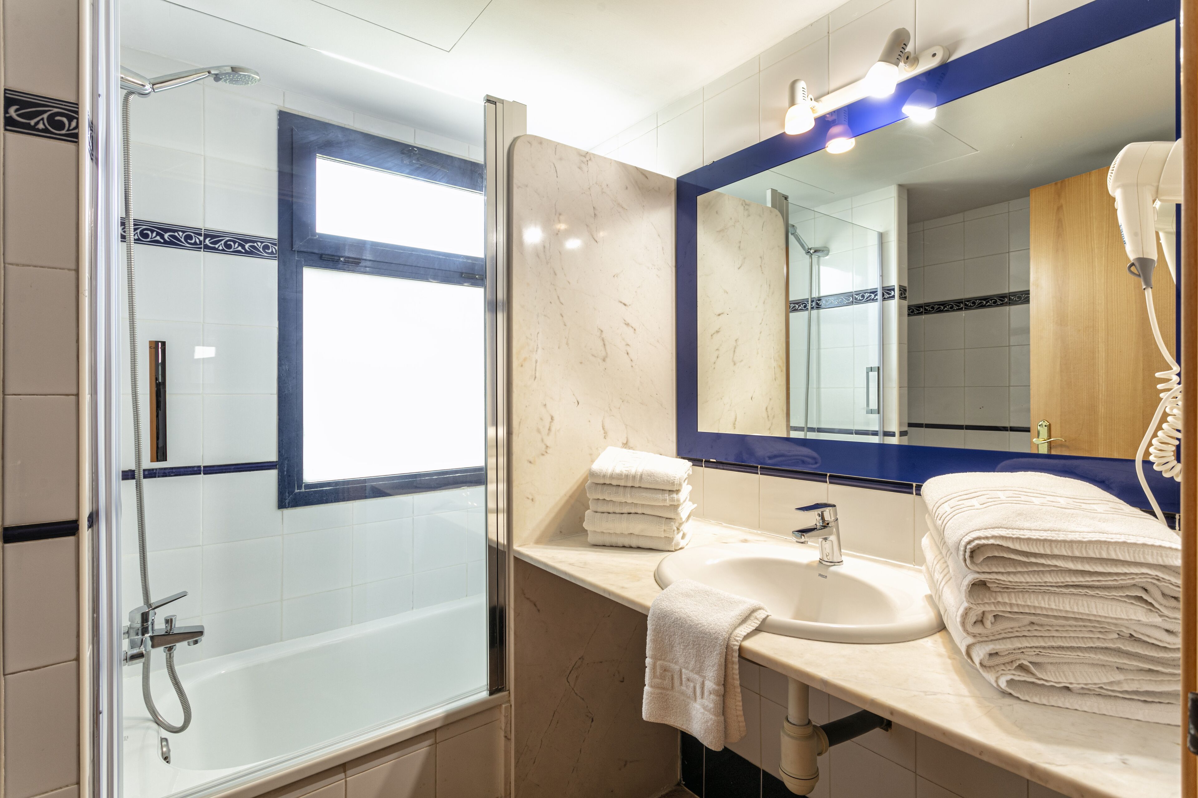 A modern bathroom with a glass-enclosed shower, a sink with a mirror, and neatly stacked towels.