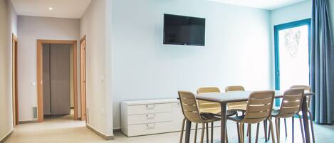 Un comedor moderno con una mesa y sillas, un televisor de pantalla plana en la pared y vistas al exterior a través de una ventana.