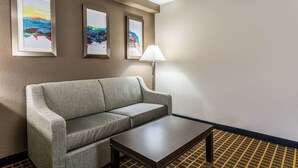 Een hotelkamer met een grijze bank, een tafeltje en drie ingelijste abstracte schilderijen aan de muur.