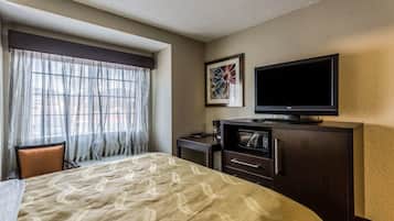 Una habitación de hotel con una cama, televisión, microondas y ventana con cortinas.