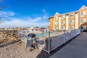 A hotel with a swimming pool, a barbecue area, and a stone wall.