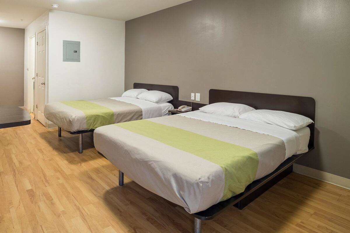 A hotel room with two single beds, wooden flooring, a door, and a light switch on the wall.
