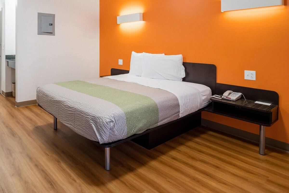 A hotel room with a bed, a bedside table with a phone, and a wall socket.