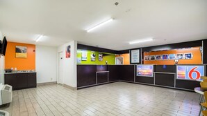 Un espace d’accueil d’hôtel comprenant un comptoir d’enregistrement, un bureau de réception et un mur orné d’affiches d’information.