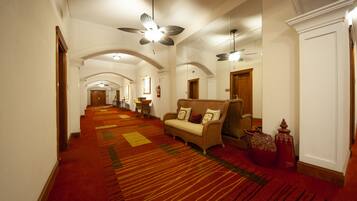 Un hall de hotel con alfombra roja, un sofá, una silla y un ventilador de techo.