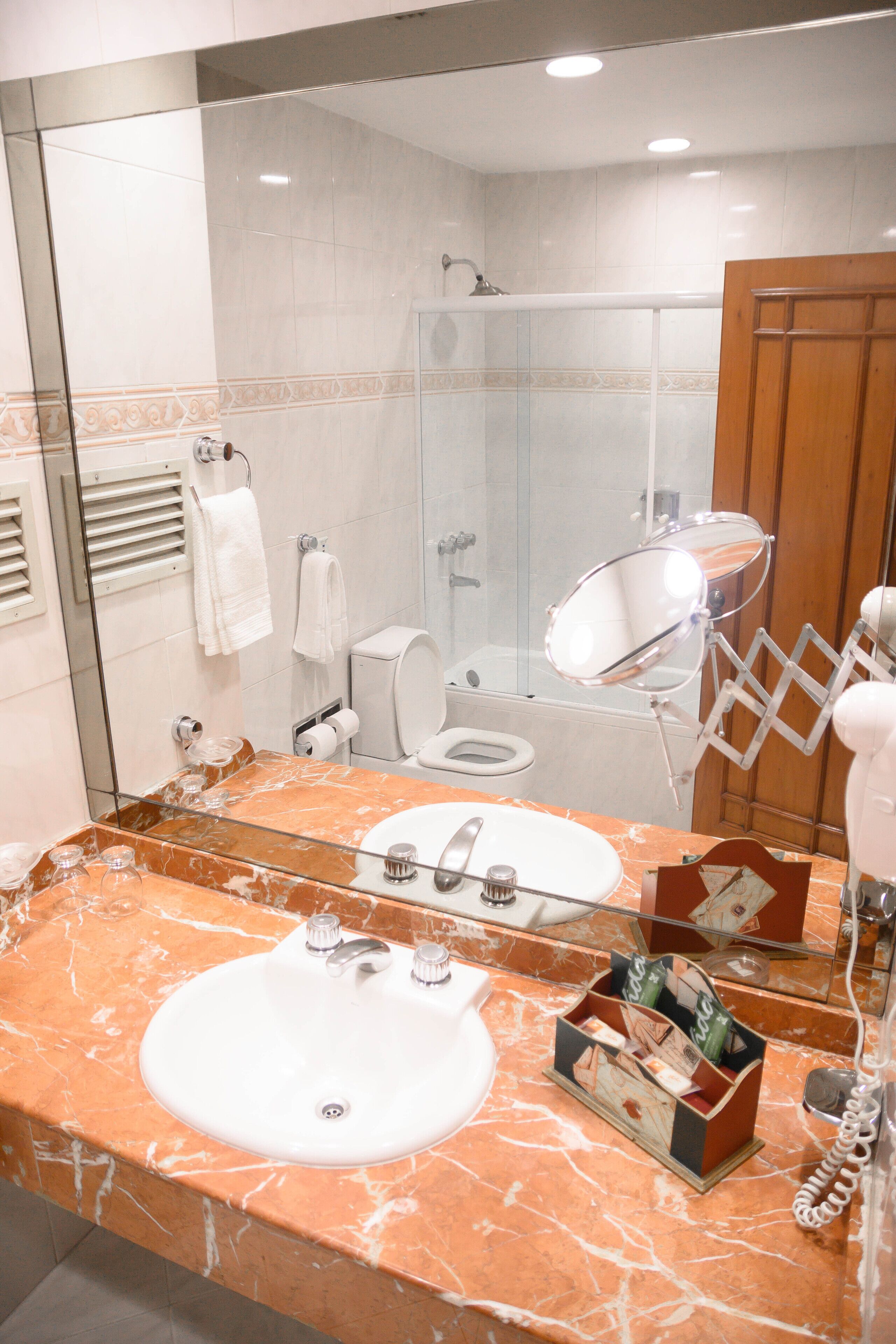 A bathroom with a marble sink, a glass shower enclosure, a toilet, and a mirror with a telephone.