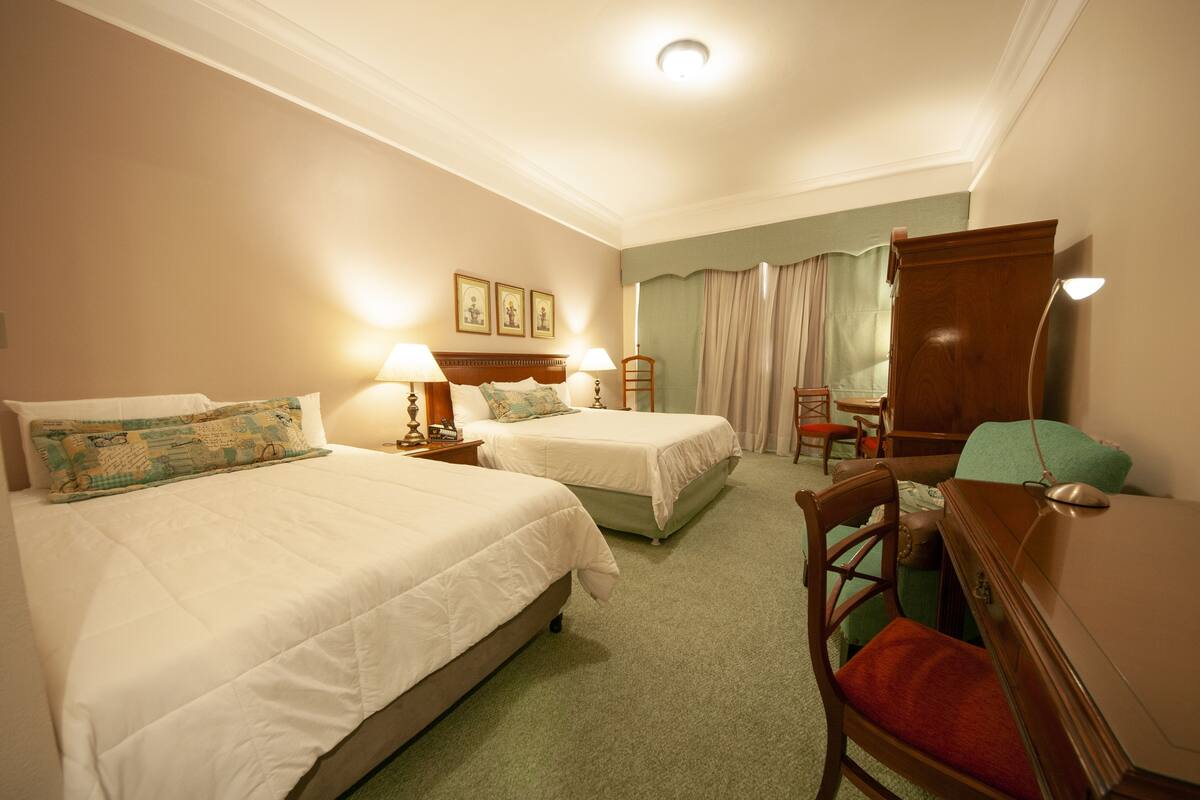 A hotel room with two beds, a desk, a chair, and a dresser.