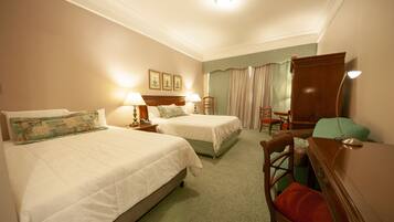 Quarto de hotel com duas camas, uma escrivaninha, uma cadeira e um aparador.