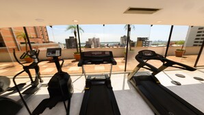 Un gimnasio con cintas de correr y equipo de ejercicio en un balcón con vista a la ciudad.
